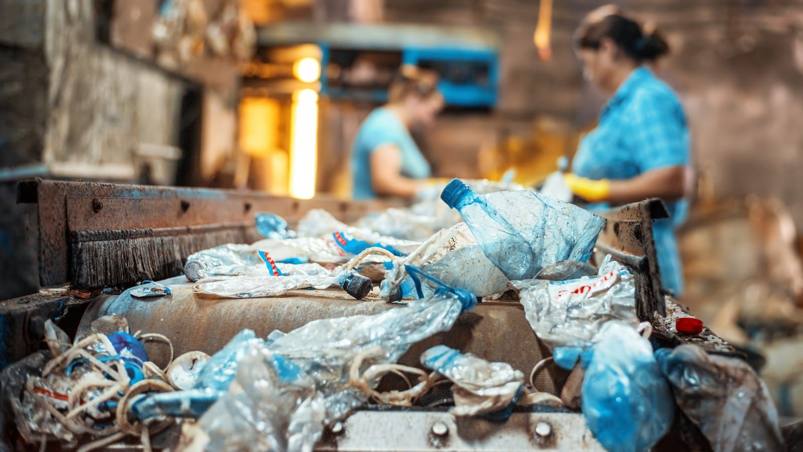 Film y envases plásticos post-consumo en la cinta de preselección de una planta de reciclaje, con operarias al fondo