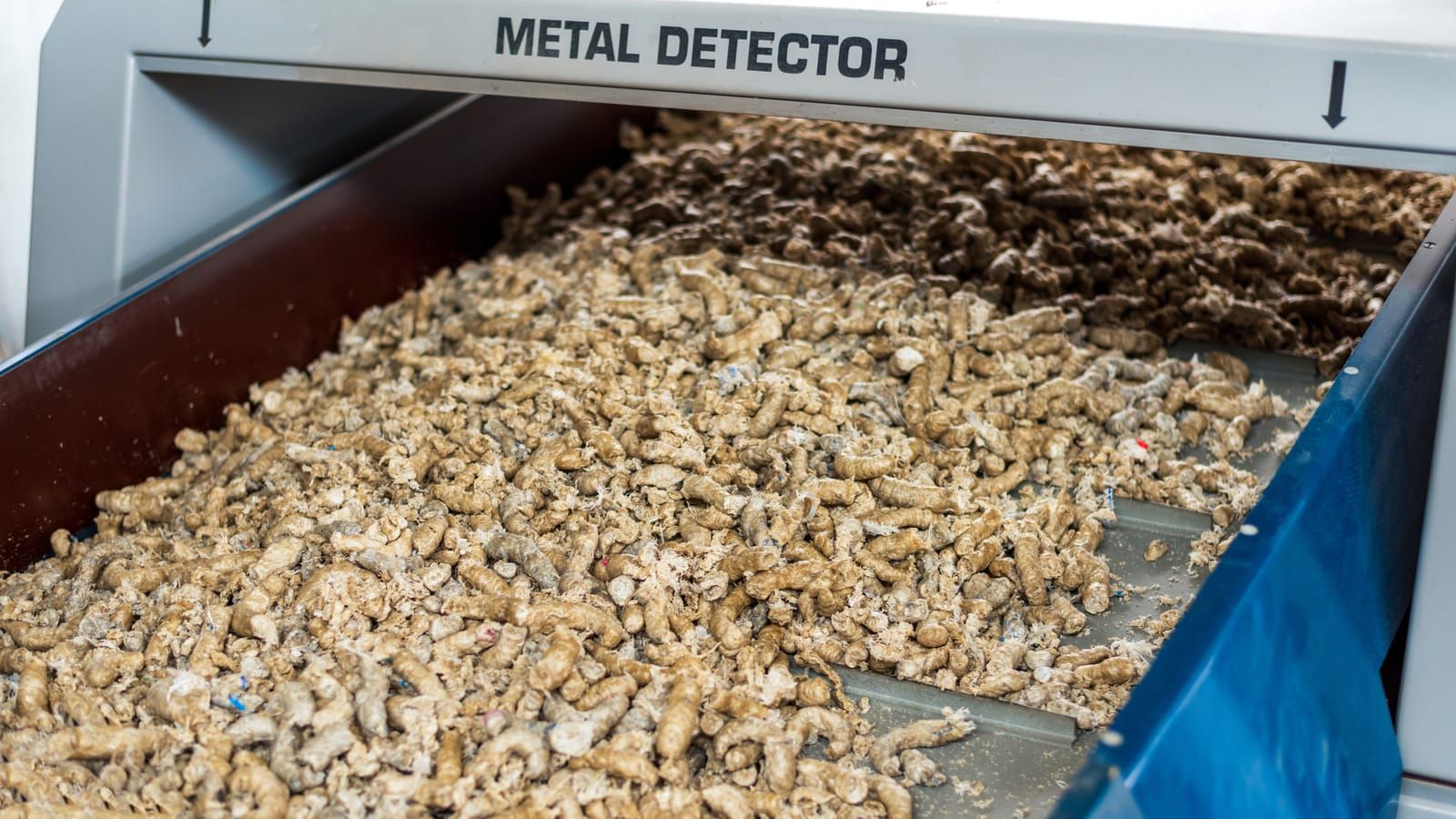 Plástico triturado avanzando por una cinta bajo un detector de metales en la entrada de una línea de lavado